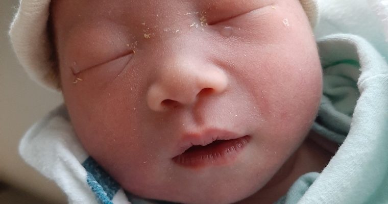 Newborn Baby C in a white hat and blue swaddle after a natural VBAC