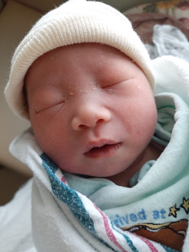 Newborn Baby C in a white hat and blue swaddle after a natural VBAC