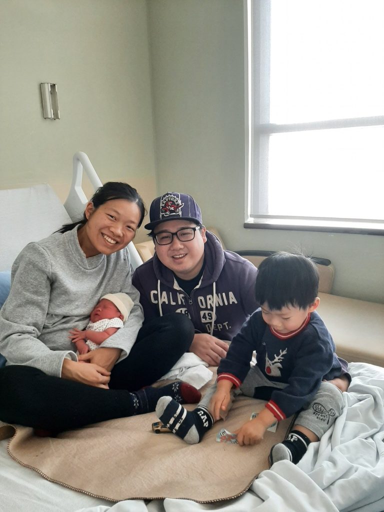 A family picture on the hospital bed with Dad, mom, Toddler boy and a newborn baby girl