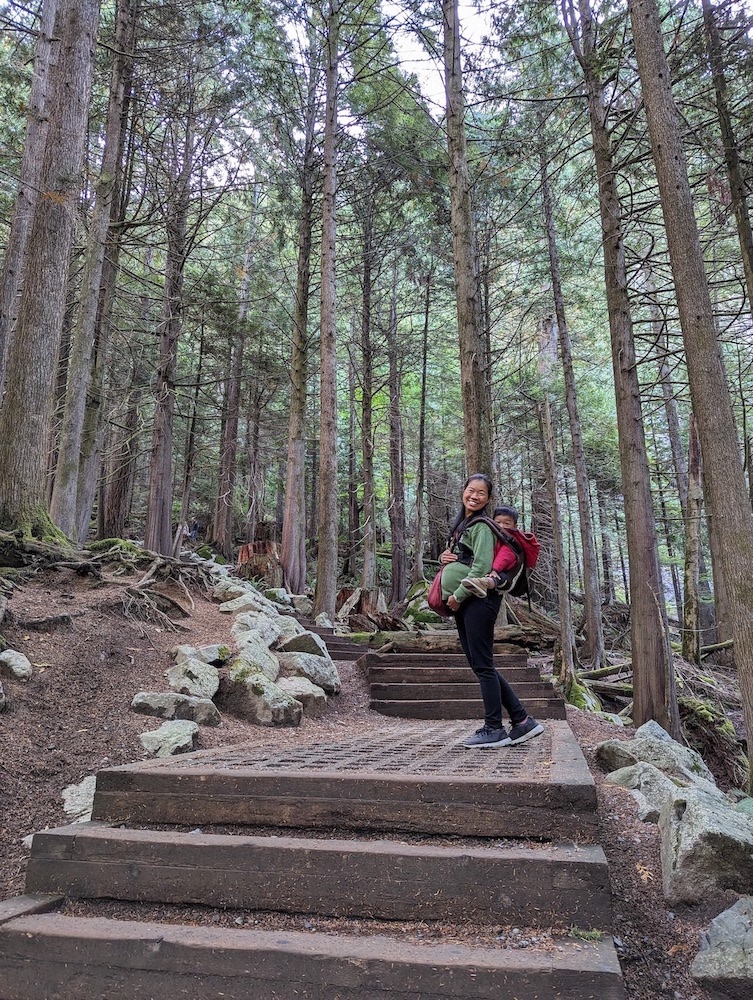 Pragnent Asian woman wearing a toddler on the back in the forest