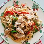 Chicken chow mein on a green edged plate with a red and white tea towel underneath