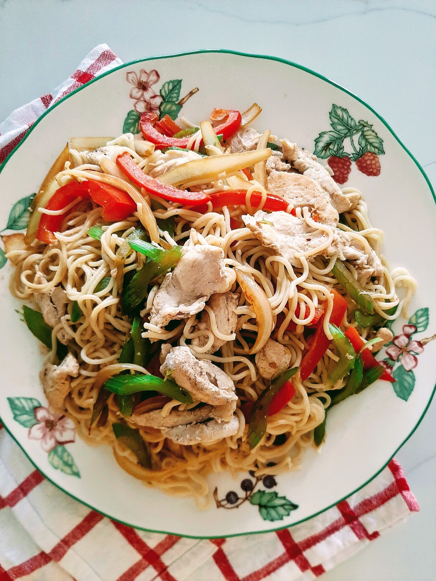 Chicken chow mein on a green edged plate with a red and white tea towel underneath