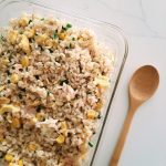 Salmon Fried rice in rectangular glass container with a wooden spoon on whilte marble countertop