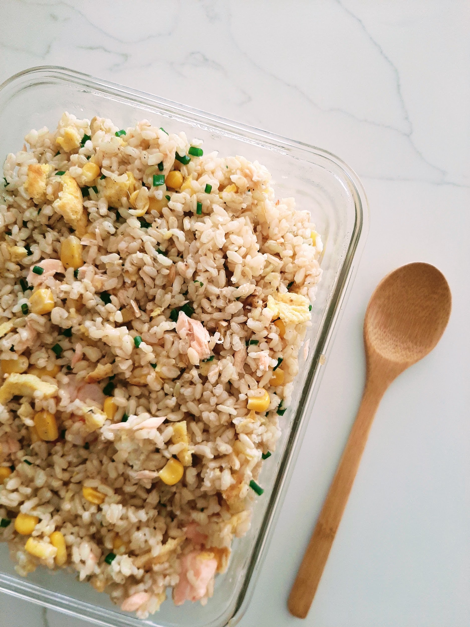 Salmon Fried rice in rectangular glass container with a wooden spoon on whilte marble countertop