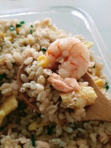 Salmon fried rice in a wooden spoon with shrimp and corn kernels